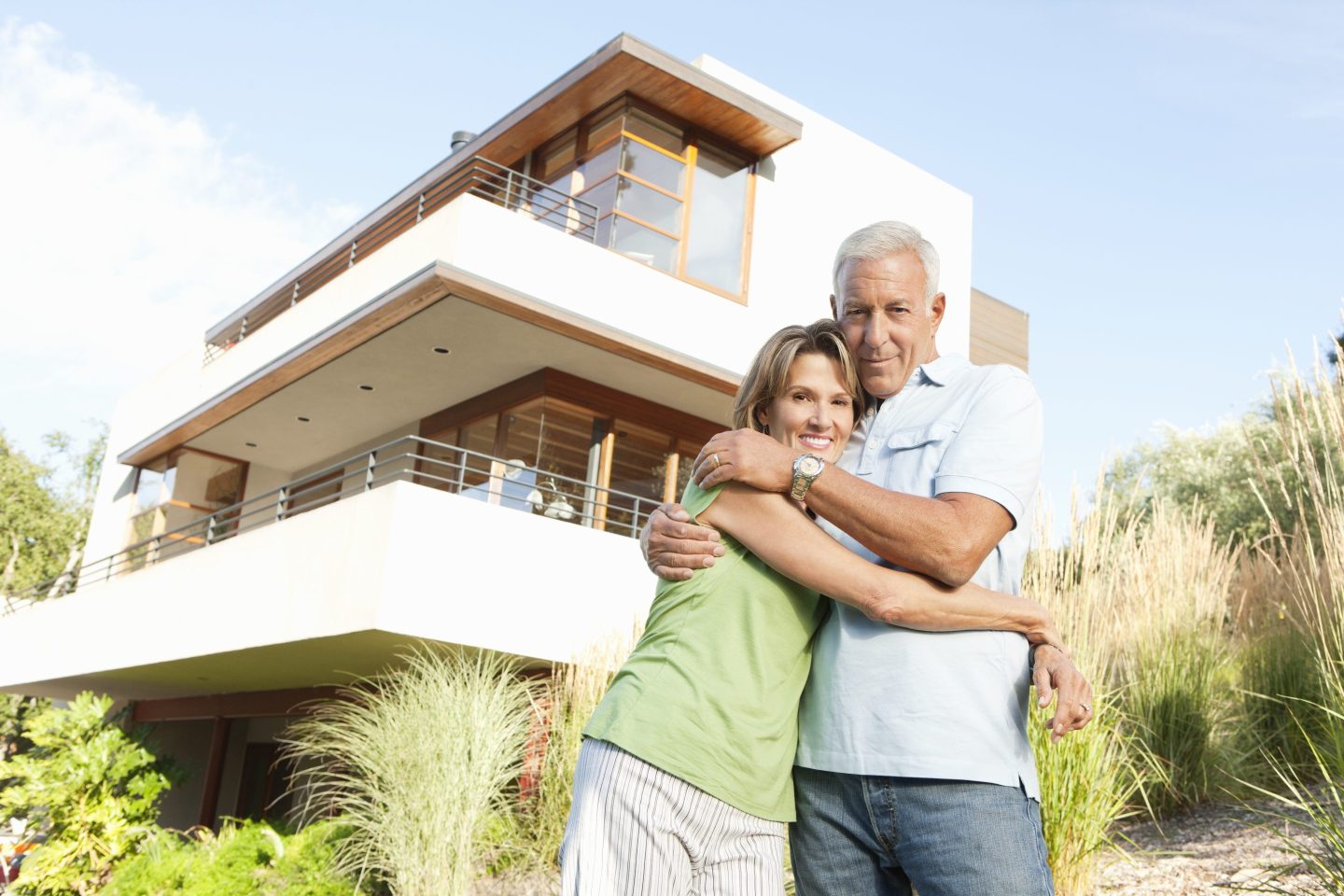 Mature couple hugging in front of modern home.